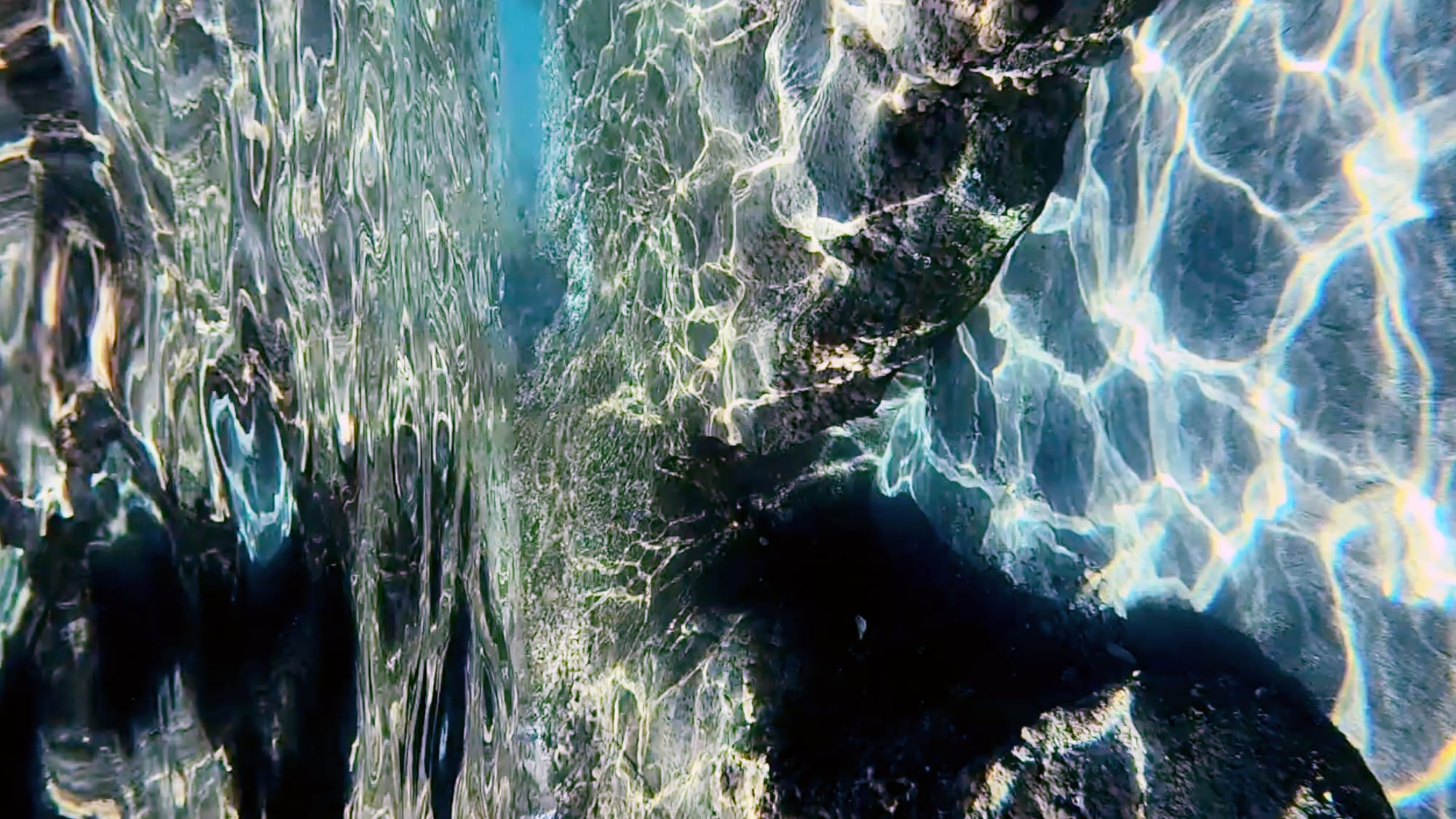 Sunlight refracted into moving lines across submerged rock.